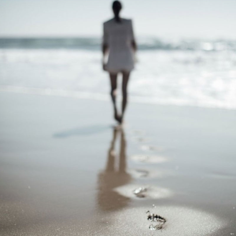 woman walking towards sea with footprints in sand